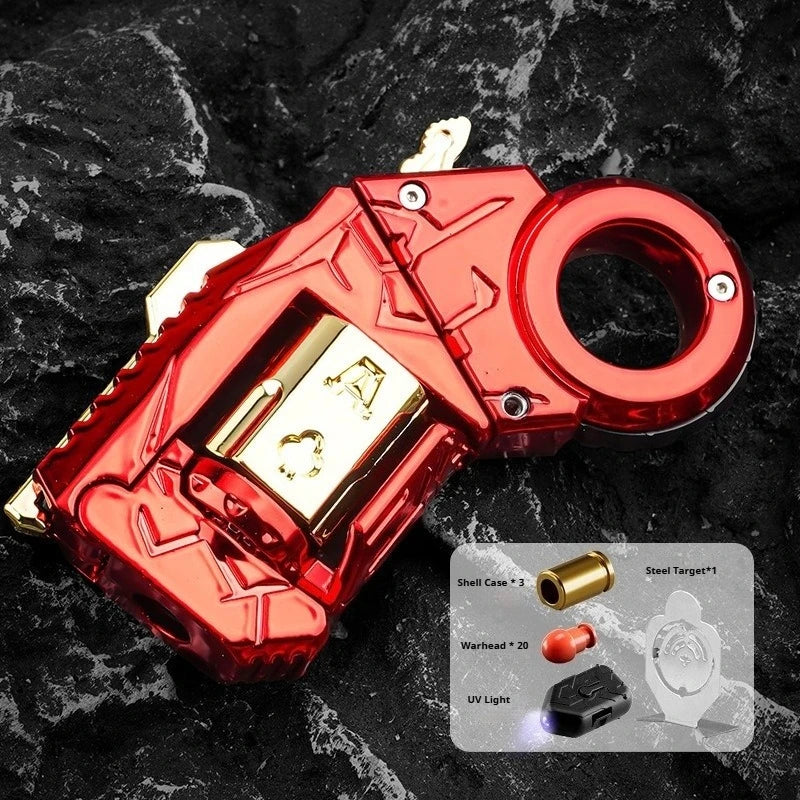 A red metal gun-shaped fidget slider key with a gold ring and various accessories is shown on a black textured surface.