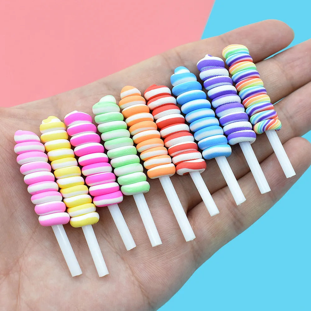 A hand holds a pack of ten colorful polymer clay marshmallow charms in various shades of pink, orange, green, and blue.