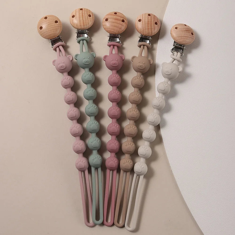 A collection of silicone bear paw pacifier clips in various pastel colors and wood accents.