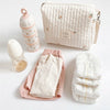 A quilted cream fabric diaper caddy organizer with attached stroller straps and a bundle of baby clothing.