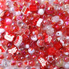 A close-up of small, colorful acrylic bow beads in various shades of red and pink scattered on a white surface.
