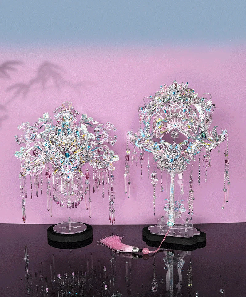 A detailed silver and iridescent phoenix coronet model kit displayed on a stand against a pink background.