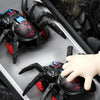 A black inertia-powered spider crawling toy car is shown in a close-up view against a dark background.