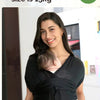 A woman is holding a baby in a black X-shaped sling carrier for newborn support.