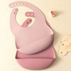 A pink silicone baby bib is shown on a light background next to a small decorative item.