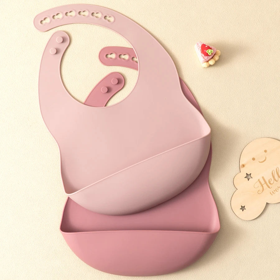 A pink silicone baby bib is shown on a light background next to a small decorative item.