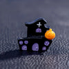 A small black figurine shaped like a house with purple accents and an orange pumpkin.