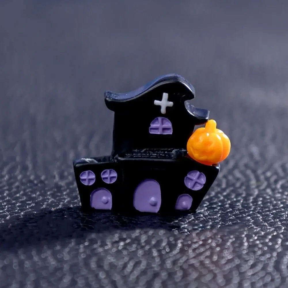 A small black figurine shaped like a house with purple accents and an orange pumpkin.