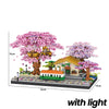 A miniature diorama featuring a pink sakura tree, a train, and a small house built from building blocks with integrated light
