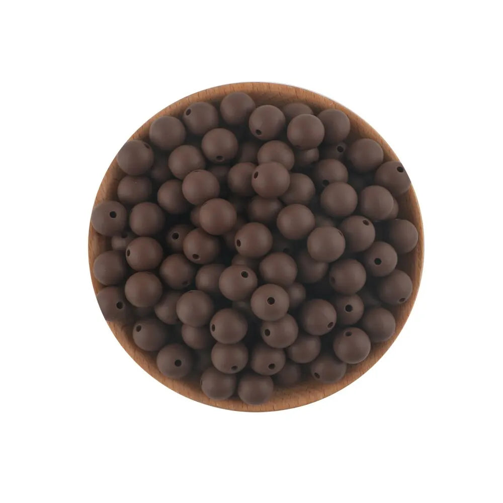 A pile of dark brown silicone round beads for jewelry making and DIY crafts resting on a wooden surface.