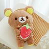A brown plush toy shaped like a bear with yellow ears, holding a red strawberry.