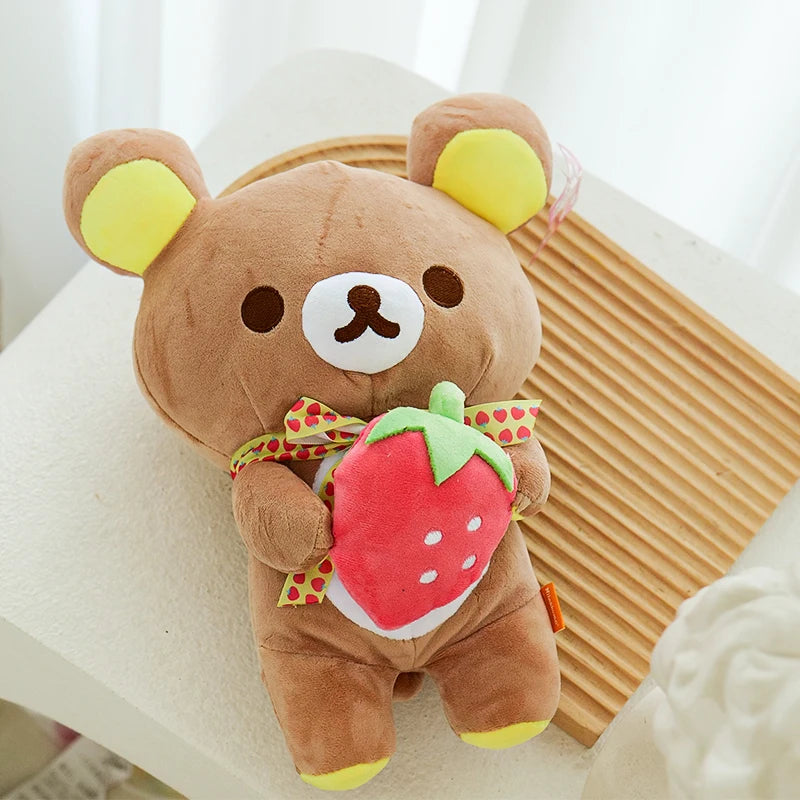 A brown plush toy shaped like a bear with yellow ears, holding a red strawberry.