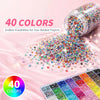 A collection of 40 colors of 3mm flatback resin jelly rhinestones and craft gems spilled onto a pink surface.