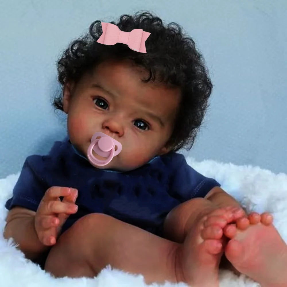 A newborn baby with curly hair wearing a dark blue top and a pink bow