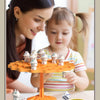 A young girl is playing with an orange frog balance tree math game featuring small frog figures and a yellow spinner.
