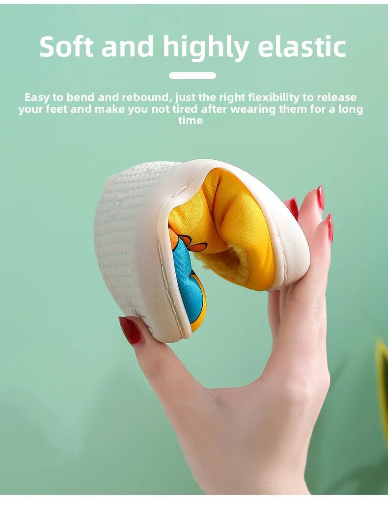 A close-up of a soft yellow and blue cartoon dinosaur plush slipper being held by a hand.