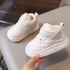A close-up of a white toddler winter snow boot with a quilted texture and soft sole being held by a hand.