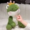 A hand gently touches a cute green frog prince plush toy with a yellow crown.
