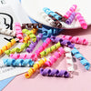 A collection of ten colorful polymer clay marshmallow charms in various shades and shapes scattered on a pink surface.