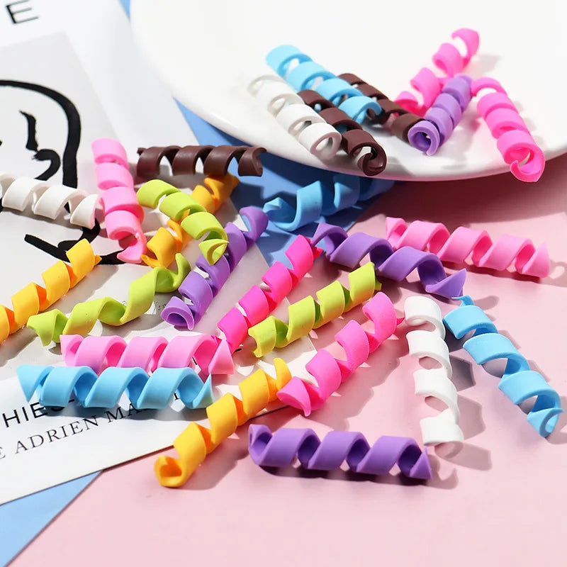 A collection of ten colorful polymer clay marshmallow charms in various shades and shapes scattered on a pink surface.
