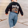 A toddler wearing a black long-sleeve shirt and blue plaid corduroy pants with a graphic print.