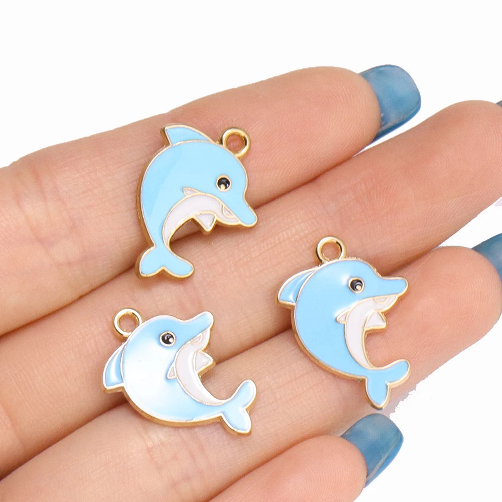 A hand holds several light blue enamel marine life charms for jewelry making