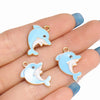 A hand holds several light blue enamel marine life charms for jewelry making