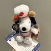 A white Snoopy plush charm with a red bow and brown accents is displayed on a white card.
