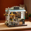 A detailed miniature wooden coffee shop house kit featuring a counter, shelves stocked with goods, and signage.