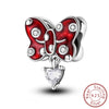 A silver butterfly charm with red enamel and clear stones, attached to a heart-shaped pendant.