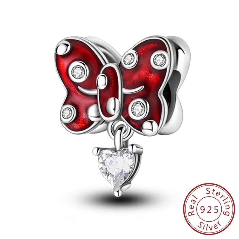 A silver butterfly charm with red enamel and clear stones, attached to a heart-shaped pendant.