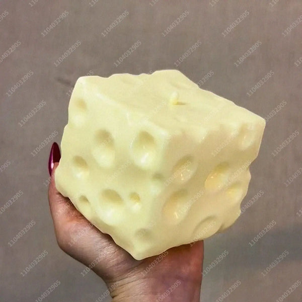 A hand holds a large, pale yellow cheese cube stress ball against a neutral background.