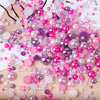 A close-up of mixed resin rhinestone pearls in shades of pink and purple scattered on a wooden surface.