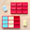 A red silicone mold tray with multiple cavities and a yellow soap bar next to it.