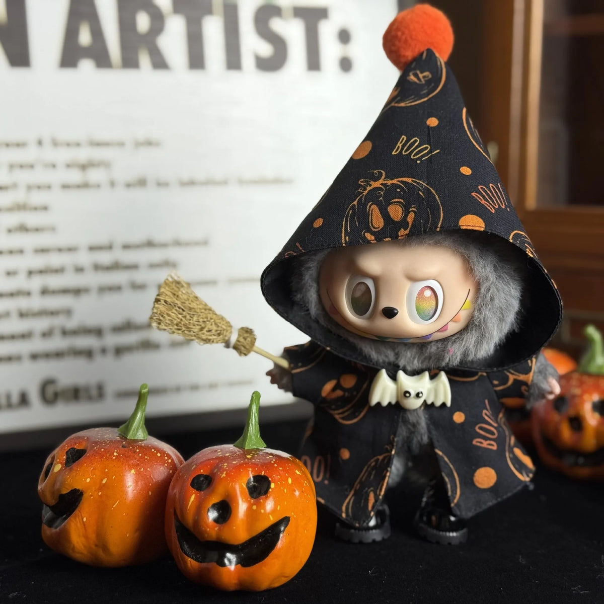 A small doll dressed as a witch with an orange pumpkin and a pointed hat sits next to several carved Halloween pumpkins.