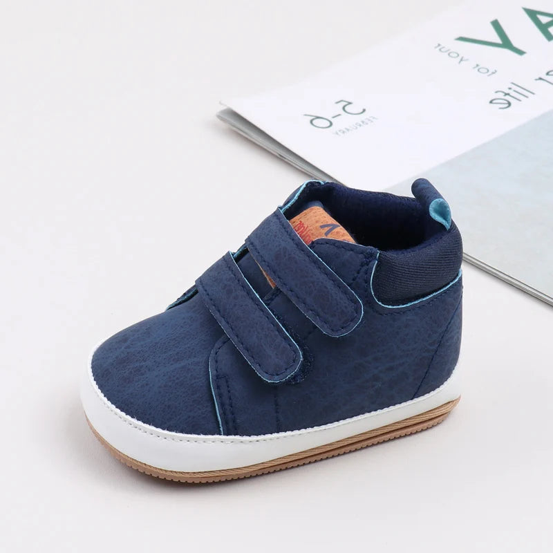 A pair of navy blue soft PU leather baby first walker shoes with a white sole resting on a light background.