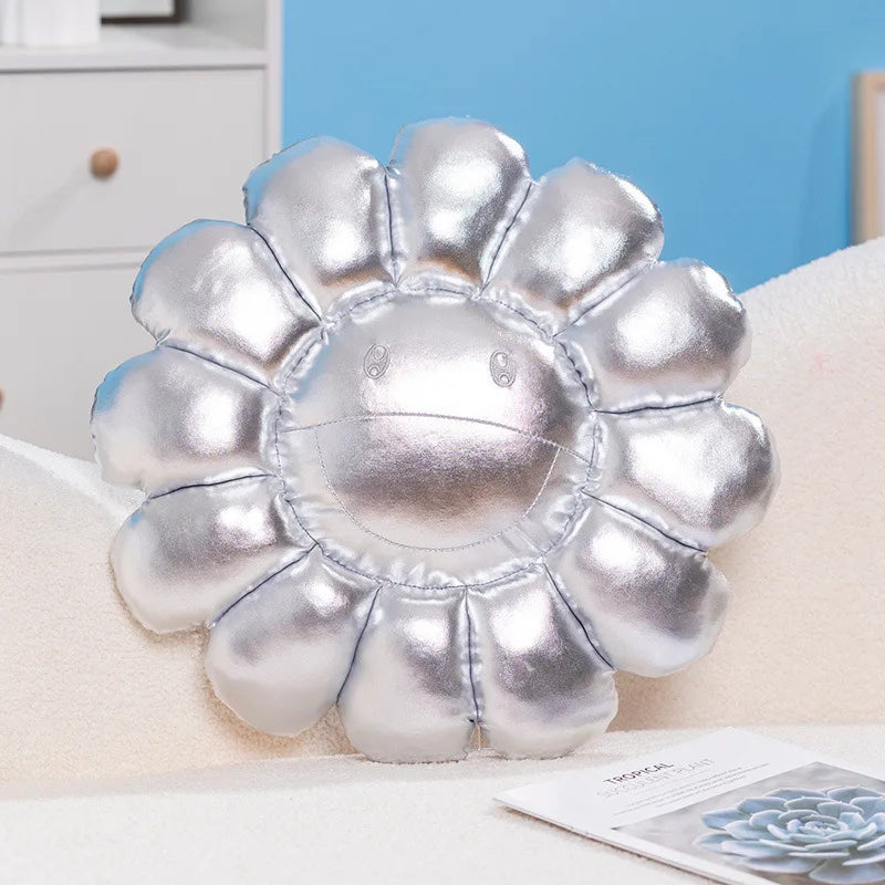 A silver plush cushion shaped like a large sunflower resting on a white surface.