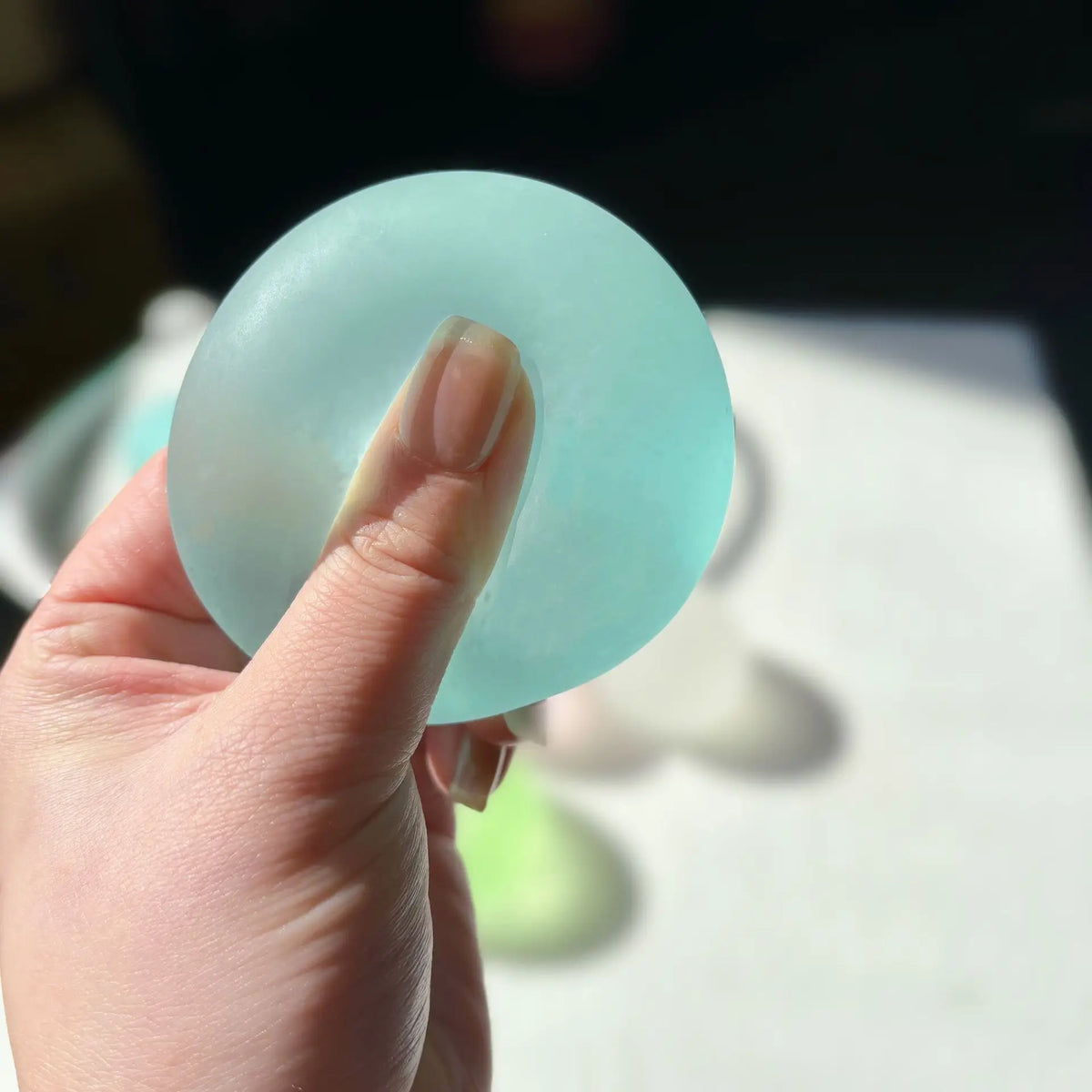 A hand holds a light blue squishy stress cube, showing its smooth, circular shape.