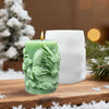 A green silicone candle mold shaped like a dragon with cloud patterns sits next to a white candle and pine greenery.
