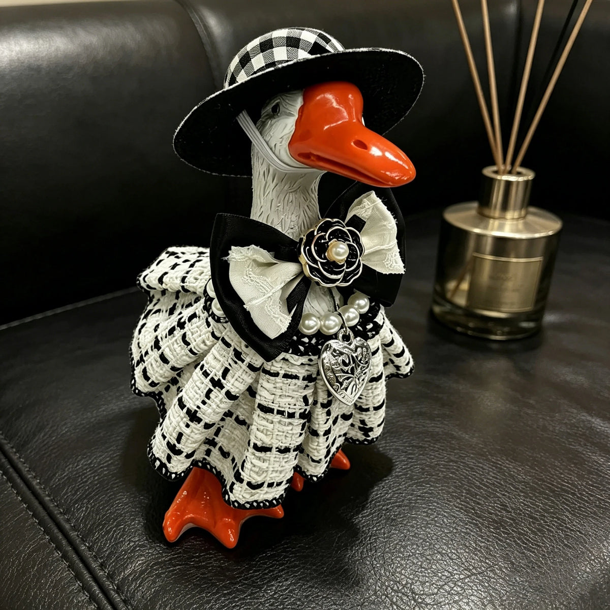 A handcrafted mini goose statue dressed in a black and white plaid outfit with a bow and pearl details.