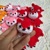 A hand holds several handcrafted crochet animal keychains in shades of pink and red.