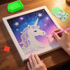 A hand paints a unicorn design on a diamond painting canvas using an ergonomic drill pen, with extra tools nearby.