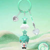 A mystery blind box figure of a character with green hair and white clothing is displayed below a silver heart-shaped charm o