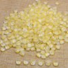 A pile of translucent yellow tulip flower glass beads scattered on a beige fabric surface.