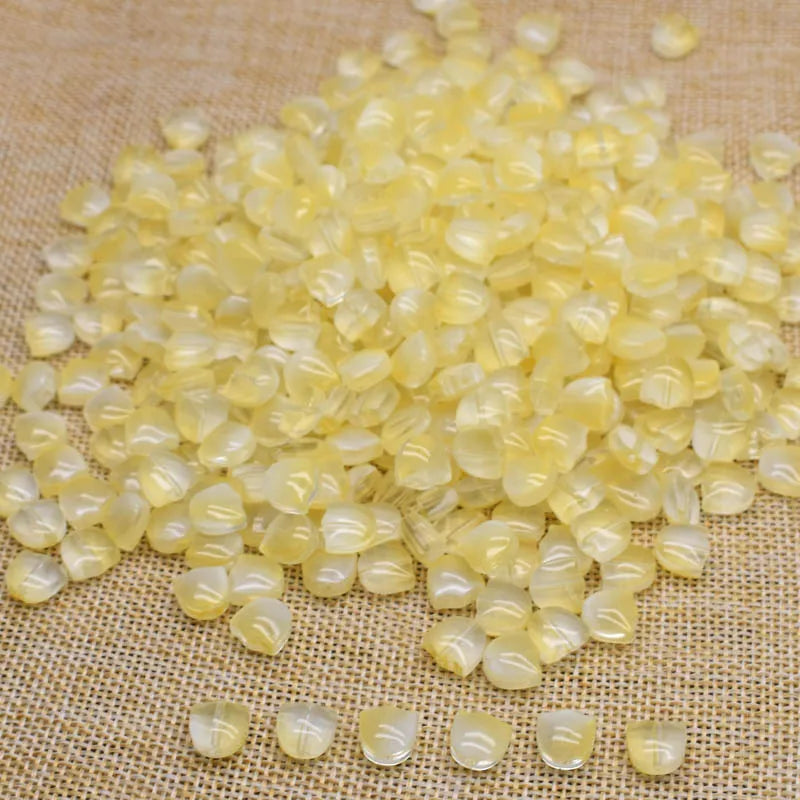 A pile of translucent yellow tulip flower glass beads scattered on a beige fabric surface.
