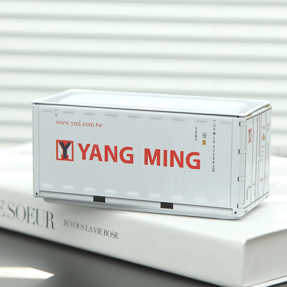 A white miniature industrial iron storage box with an openable lid resting on a white book.
