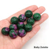 A hand holds several green and purple crystal spheres, identified as Ruby Zoisite.