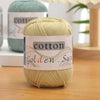 A ball of light beige cotton knitting yarn labeled Golden Sun is displayed on a wooden surface.
