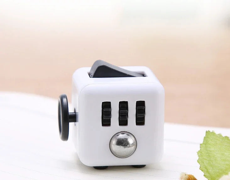 A white fidget cube with a rotating joystick and magnetic buttons resting on a white surface.