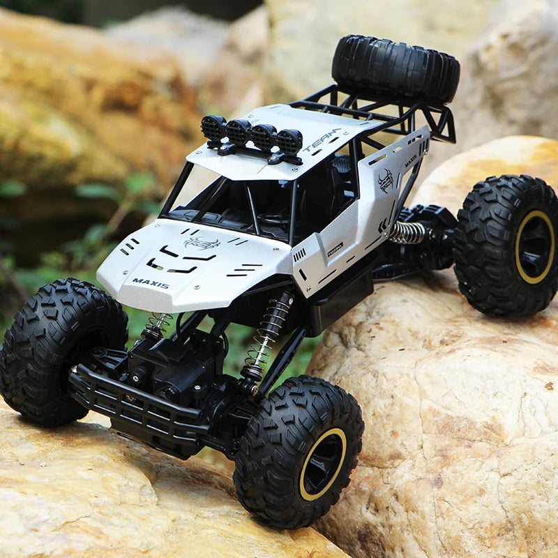 A silver and black high-speed 4WD off-road RC truck with large tires resting on a light-colored rock.